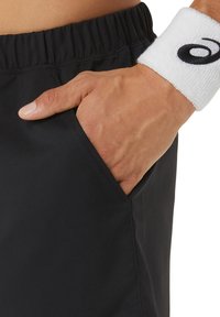 Schwarze Sportschorts mit einem weichen, strukturierten Bund und Seitentasche, ergänzt durch ein weißes Frottee-Schweißband mit einem Logo.