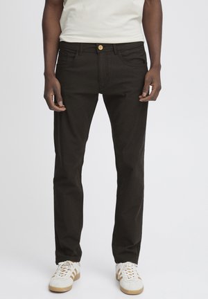 Jean noir en denim, avec une coupe droite, deux poches avant et une fermeture à bouton, porté avec des baskets blanches.