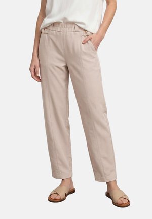 Pantalon beige taille haute avec taille élastique, poches latérales, porté avec un haut blanc et des sandales beiges à enfiler sur une personne.