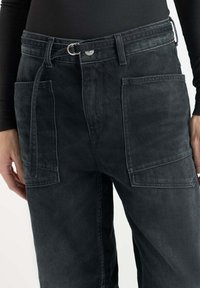 Pantalons en denim noir avec une taille haute, une coupe large et deux grandes poches avant. Comprend une ceinture avec une boucle en métal et une finition texturée globale.