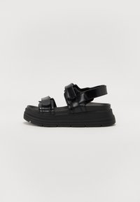 Sandalias de plataforma negras hechas de material brillante, con correas anchas y una suela acolchada con dibujo para agarre. Correa trasera ajustable.