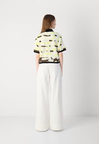 Short-sleeve top in white, yellow, and brown abstract pattern with black trim; paired with wide-leg white trousers; casual design.