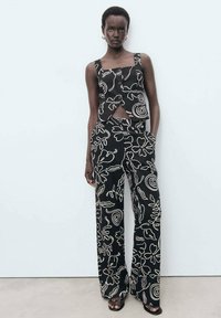 Ensemble noir en deux pièces comprenant un haut sans manches avec une découpe et un pantalon large, tous deux ornés de motifs floraux abstraits et de spirales blanches.