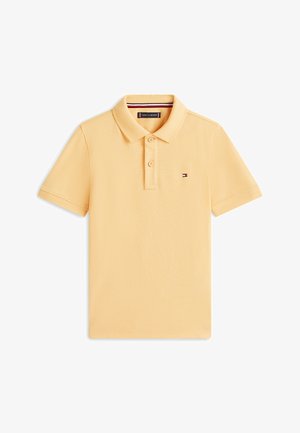 Żółta koszulka polo z krótkim rękawem, z dwoma guzikami, małe logo flagi Tommy Hilfiger na piersi oraz ściągacz na kołnierzu z czerwonym, białym i niebieskim wykończeniem.