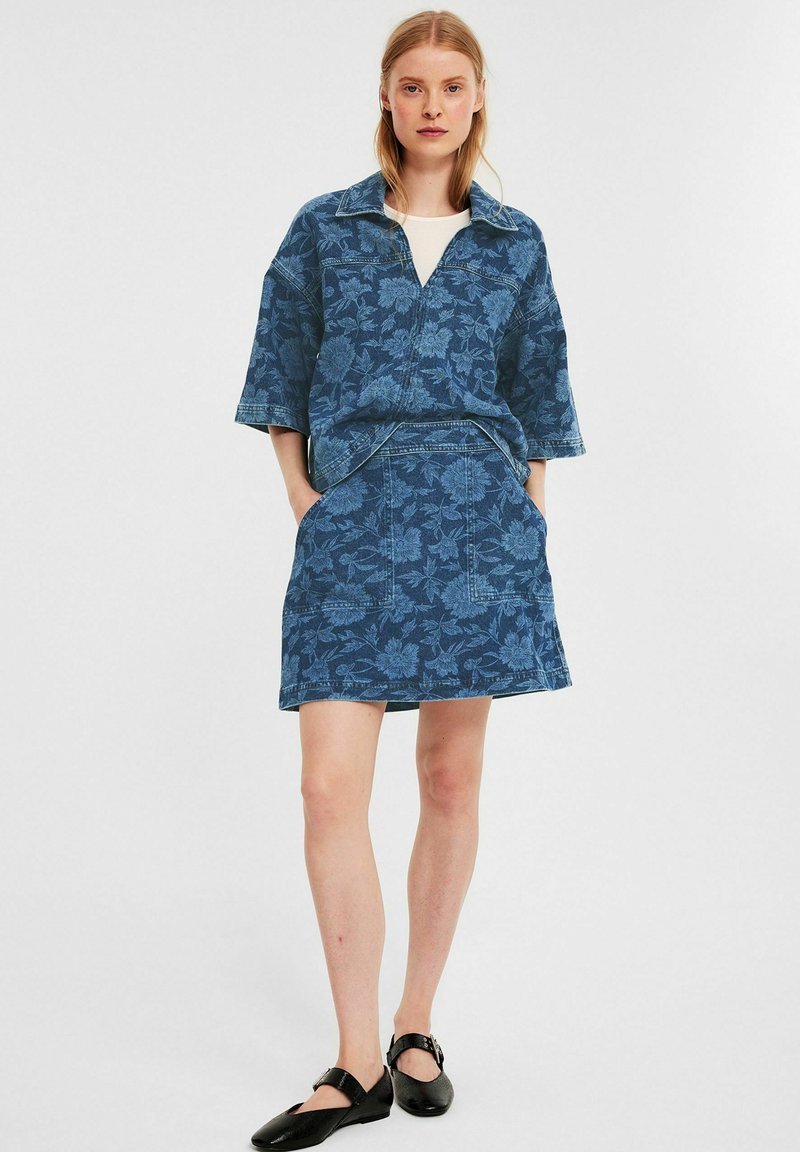 Jeansoutfit med blommönster, kortärmad skjorta med krage och matchande kjol med fickor, i en blå färgskala.
