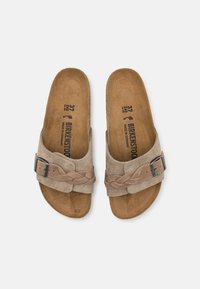 Sandali in suede beige chiaro con cinturino intrecciato e fibbia argentata, suola piatta e soletta in pelle con logo stampato e dettagli sulla taglia.