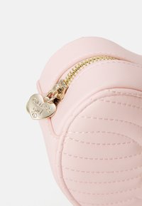 Pochette in finta pelle rosa con forma arrotondata, texture trapuntata, zip dorata e tirante a forma di cuore in metallo con la scritta "GUESS girl".