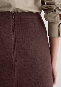 Bordeaux wollen rok met een gestructureerde afwerking, middelhoge taille en naaddetails. Gepaard met een lichtbeige top met opgerolde mouwen.