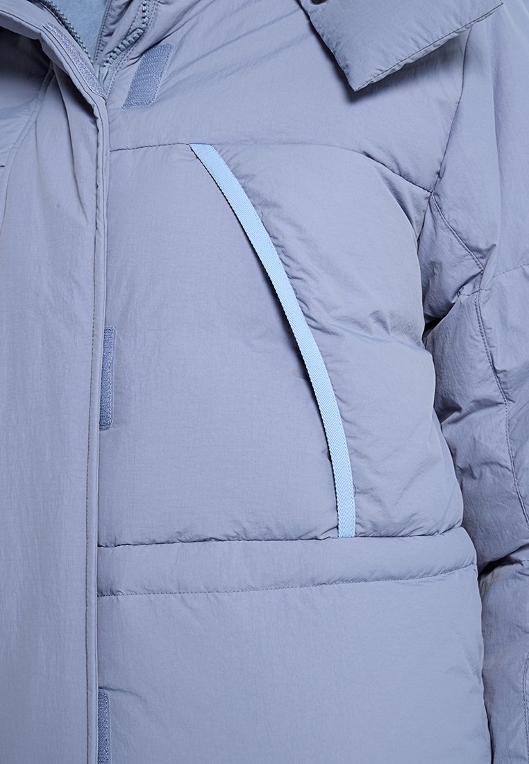 Giubbotto imbottito grigio chiaro con una superficie liscia, caratterizzato da cuciture blu a contrasto, una chiusura frontale con zip e un colletto alto per l'isolamento.