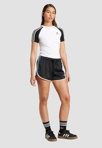 Vit och svart kortärmad skjorta med tre svarta ränder, parat med svarta träningsshorts med rosa kant och flerfärgade sidostripes.