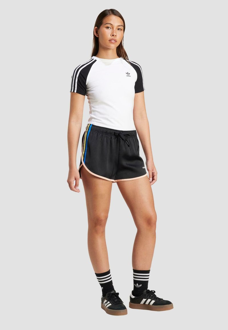 Weißes und schwarzes Kurzarmhemd mit drei schwarzen Streifen, kombiniert mit schwarzen Sportshorts mit pinkem Saum und mehrfarbigen seitlichen Streifen.