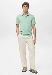 Polo shirt verde chiaro a maniche corte con colletto, abbinato a pantaloni color crema e sandali marroni con cinturini. Tessuto liscio, fit casual.