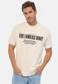Camiseta de algodón color crema con texto en negrita negro: "¿GUERRA DE CINCO FAMILIAS?" y texto adicional, con un corte relajado y mangas cortas.