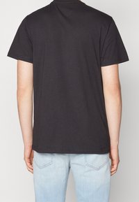 Camiseta de algodón negra con mangas cortas, que presenta una parte trasera lisa. Combinada con jeans de denim azul claro, que tienen un acabado desgastado y costuras visibles.