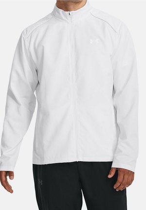 Mann trägt weiße, durchgehende Sportjacke mit langen Ärmeln und schwarze Hose, steht mit entspannten Armen an den Seiten.