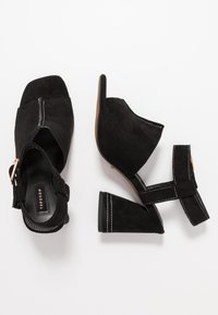 Svarta mocka öppen-tå blockklack sandaler med ankelremmar, vit sömnad och guldspännen, visade från ovan- och sidan.