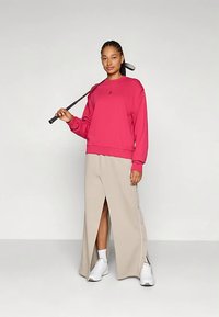 Sweatshirt rosa com mangas compridas e decote redondo, combinada com saia maxi bege com fendas laterais e detalhes de botões. Ténis brancos.