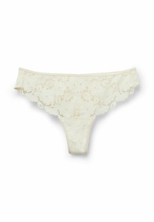 Beżowe stringi z koronką w kwiatowy wzór i ząbkowanymi krawędziami na białym tle.