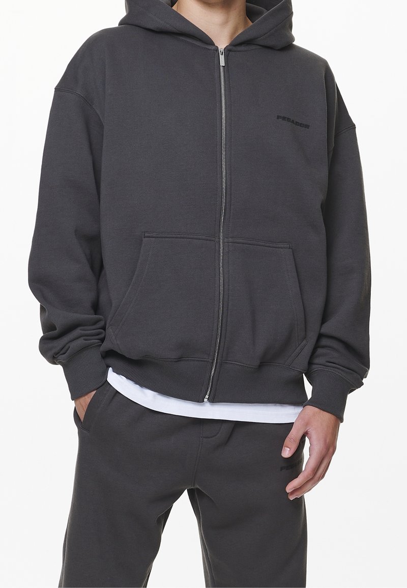Hoodie zippé gris foncé en mélange de coton, avec une poche à l'avant, des poignets côtelés et un logo discret sur la poitrine.
