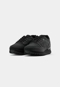 Zapatillas deportivas negras con una combinación de superficies texturizadas y lisas, diseño de cordones, cuello acolchado y suela de goma con patrón de agarre.