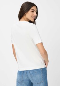 Witte korte mouwen top met een ronde halslijn, met een gladde textuur en een ontspannen pasvorm, gedragen met blauwe denim jeans in een casual omgeving.