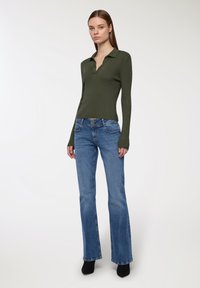 Zielono-oliwkowa, prążkowana koszulka polo z długim rękawem, zestawiona z jasnoniebieskimi dżinsami w kształcie dzwonów z zapięciem na guziki i ozdobnym przeszyciem. Czarne buty na obcasie.