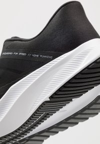 Zwarte Nike hardloopschoen met een gestructureerde bovenkant, witte tussenzool en een gegroefde rubberen buitenzool. Toont de tekst "Powered for speed."