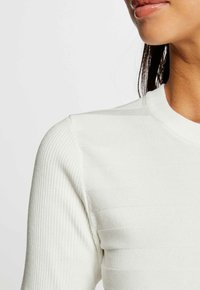 Witte geribbelde top met een ronde halslijn, textuurstrepen en aansluitende mouwen, ontworpen voor een soepele, lichte uitstraling.