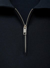 Námořnický pulovr s jemným žebrováním a polo-zip designem, který má stříbrný zip a límec. Tkanina má hladkou strukturu.