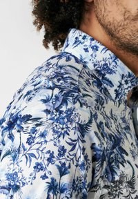 Bluse mit Blumenmuster in Blau-weiß-Farbschema; aus einem Stoff mit glatter Textur und klassischem Kragen.