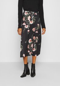 Černá midi sukně s květinovým vzorem, na které jsou růžové a bílé květiny, vyrobená z jemné tkaniny s hladkým povrchem, doplněná černými kotníkovými botami.