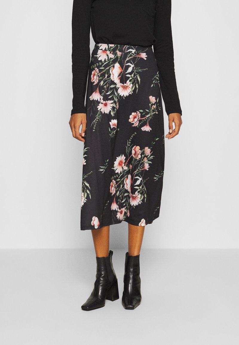 Černá midi sukně s květinovým vzorem, na které jsou růžové a bílé květiny, vyrobená z jemné tkaniny s hladkým povrchem, doplněná černými kotníkovými botami.