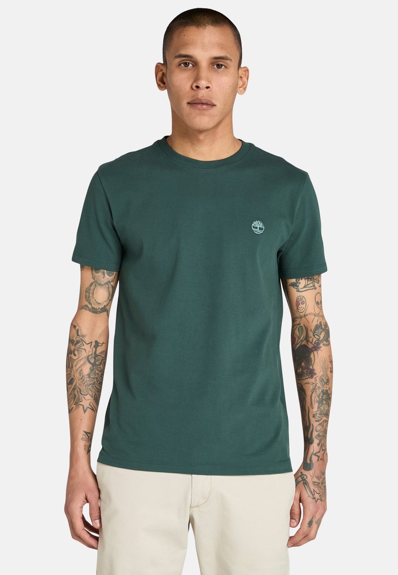 Tmavě zelené bavlněné tričko s kulatým výstřihem, krátkými rukávy a jemným logem na hrudi. Hladká textura, bez vzorů nebo akcentů.