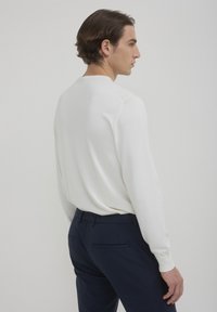 Maglione bianco lavorato a maglia con girocollo e maniche lunghe, abbinato a pantaloni navy scuri con tasca sul retro. Texture liscia.