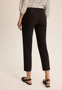 Czarne spodnie o długości do kostek, o gładkiej fakturze, dopasowanym kroju i średnim stanie, w połączeniu z płaskimi czarnymi butami wsuwanymi.