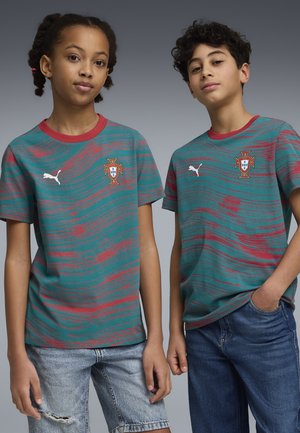 To børn iført grønne og røde Portugal fodboldtrøjer med mønster, den ene i denimshorts og den anden i blå jeans, stående side om side.