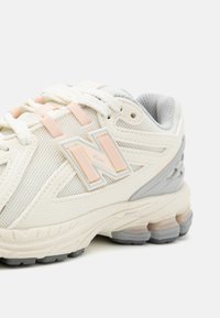 Baskets de course avec une tige en maille de couleur blanc cassé, ornées de détails en rose pâle et gris. Semelle épaisse notable avec des éléments de rembourrage.