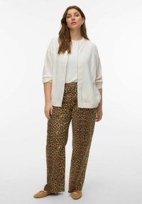 Veste légère crème à fermeture éclair sur un haut blanc, associée à un pantalon large imprimé léopard marron et des chaussures plates marron.