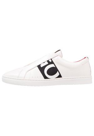 White low-top sneaker with black elastic strap displaying partial large white letters, smooth leather upper, and flat white sole.