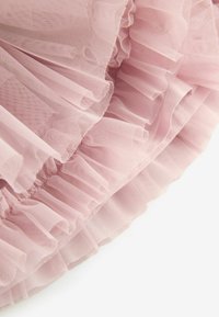 Tessuto tulle di un delicato rosa chiaro con strati di volant, caratterizzato da una consistenza morbida e trasparente e un bordo ondulato lungo il fondo.