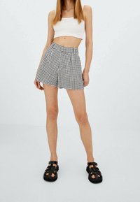 Pantalones cortos de cuadros en blanco y negro con pliegues, combinados con un top corto de canalé blanco y sandalias negras con tiras.