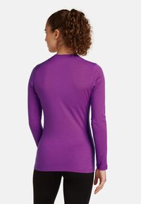 Maglietta sportiva a maniche lunghe di un vivido colore viola, con un design aderente, texture liscia e cuciture minime per un comfort migliorato.
