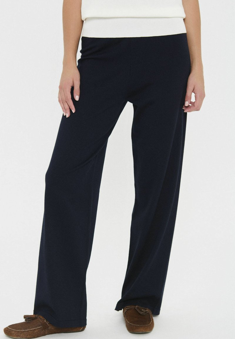 Sötétkék, bő szabású nadrág, amely puha anyagból készült, sima tapintású, rugalmas derékpánttal és kényelmes fazonnal rendelkezik.