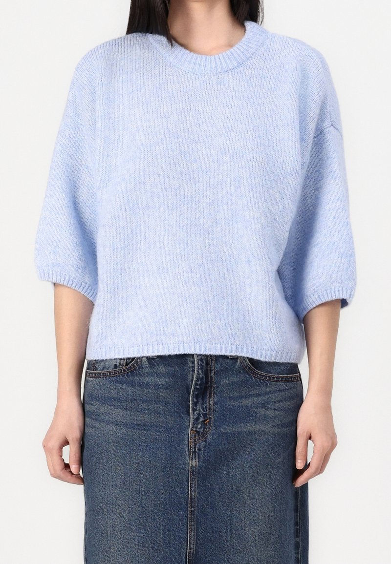 Pull tricoté bleu clair avec manches courtes et larges et un col rond, associé à une jupe en jean. Texture douce partout.