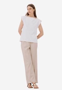 Top bianco senza maniche con spalline larghe e dettagli con bottoni abbinato a pantaloni beige chiaro a gamba larga e sandali flat. Tessuto liscio e strutturato.