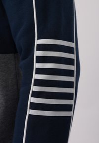 Μανίκι σε ναυτικό μπλε με λευκές οριζόντιες ρίγες και λευκή κάθετη διακόσμηση piping σε σκούρο ένδυμα με γκρι φόντο.