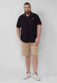 Zwarte poloshirt met witte streepaccenten, gecombineerd met beige shorts en witte sneakers. Eenvoudig ontwerp, casual pasvorm en zachte textuur.