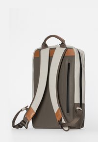 Zaino marrone e color crema con spalline regolabili imbottite, maniglia superiore, tasca laterale con zip e texture liscia.