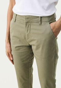 Pantaloni din bumbac khaki, cu croi slim, fața plată și buzunare laterale. Țesătura are o textură netedă și un design minimalist.