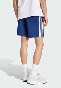 Blauwe sportshorts hebben witte zijkanten, een relaxte pasvorm en worden gecombineerd met lichtgekleurde sneakers en witte crew-sokken.